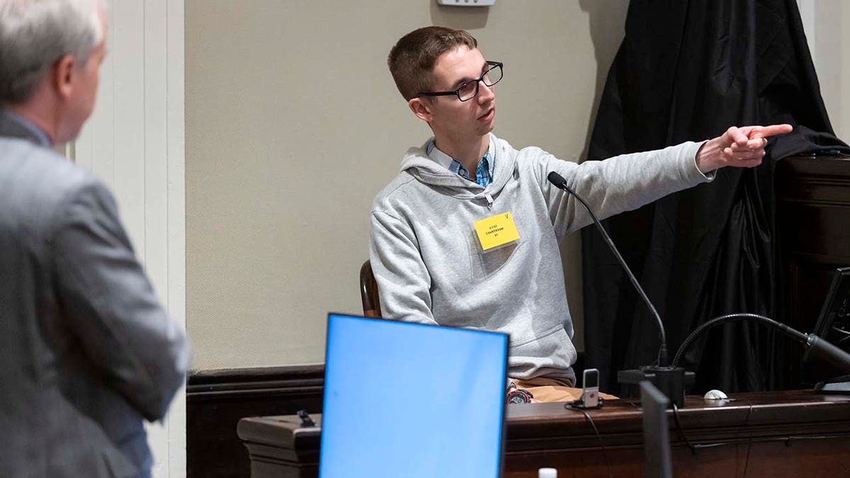 A man testifies while on the witness stand inside a courtroom.