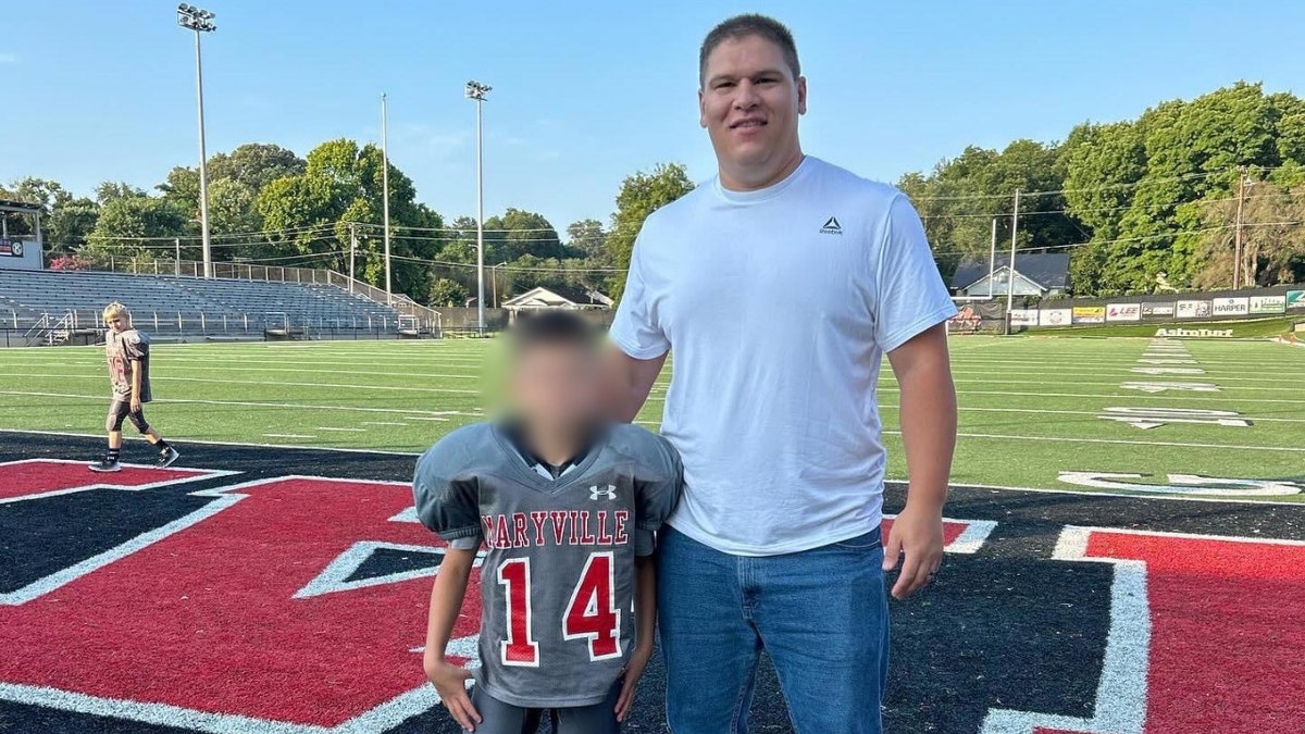 Josh Sullivan stands with his son, wearing a football uniform, on a football field in Tennessee