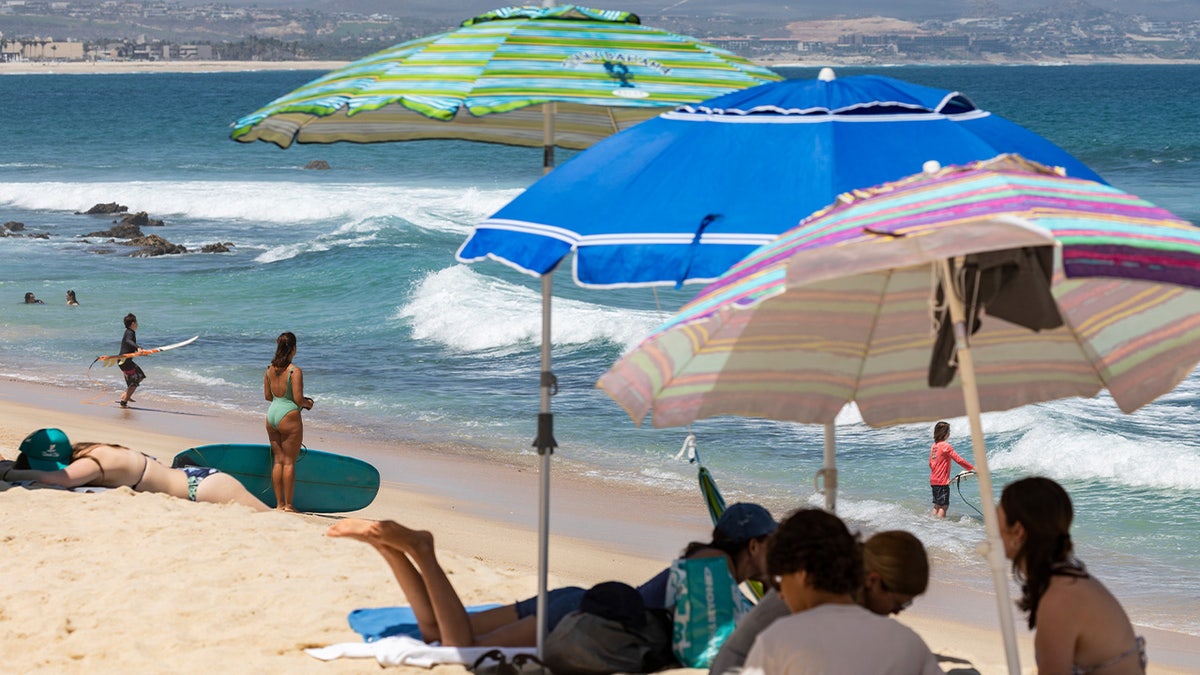 Surfers and tourists enjoying the waves. Blue, green and pink beach umbrellas planted in the sand as tourists enjoy Mexico's sunshine.