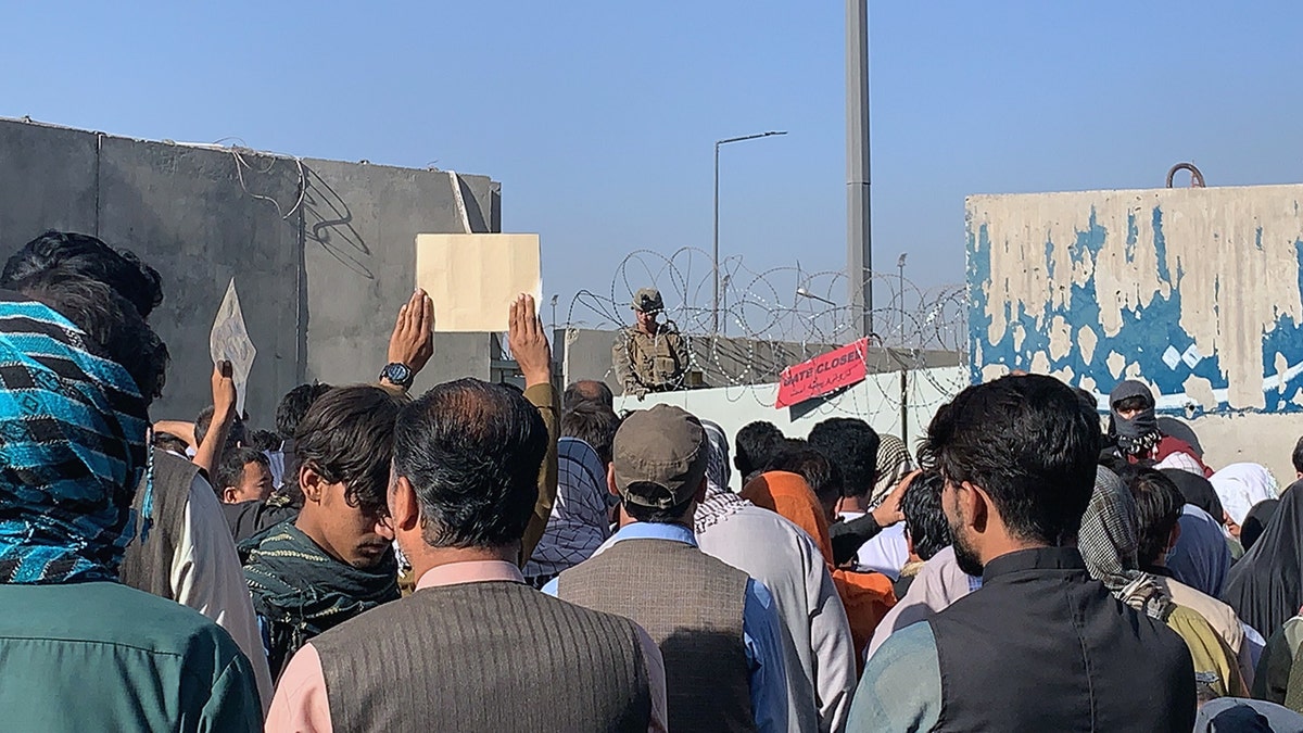 Crowd of Afghans holding papers stands before U.S. soldiers at a barricaded Kabul airport gate during the 2021 withdrawal from Afghanistan