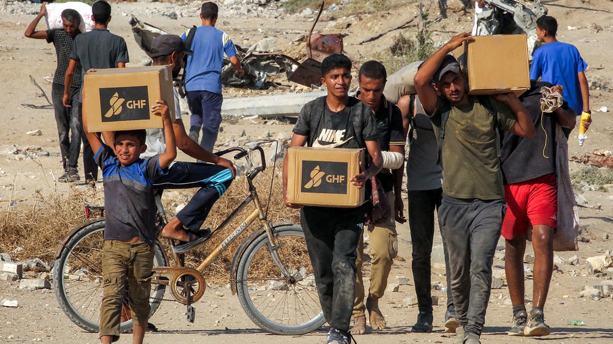 Gazans walk with boxes of humanitarian aid they received at a distribution center run by the U.S.- and Israeli-backed Gaza Humanitarian Foundation (GHF).