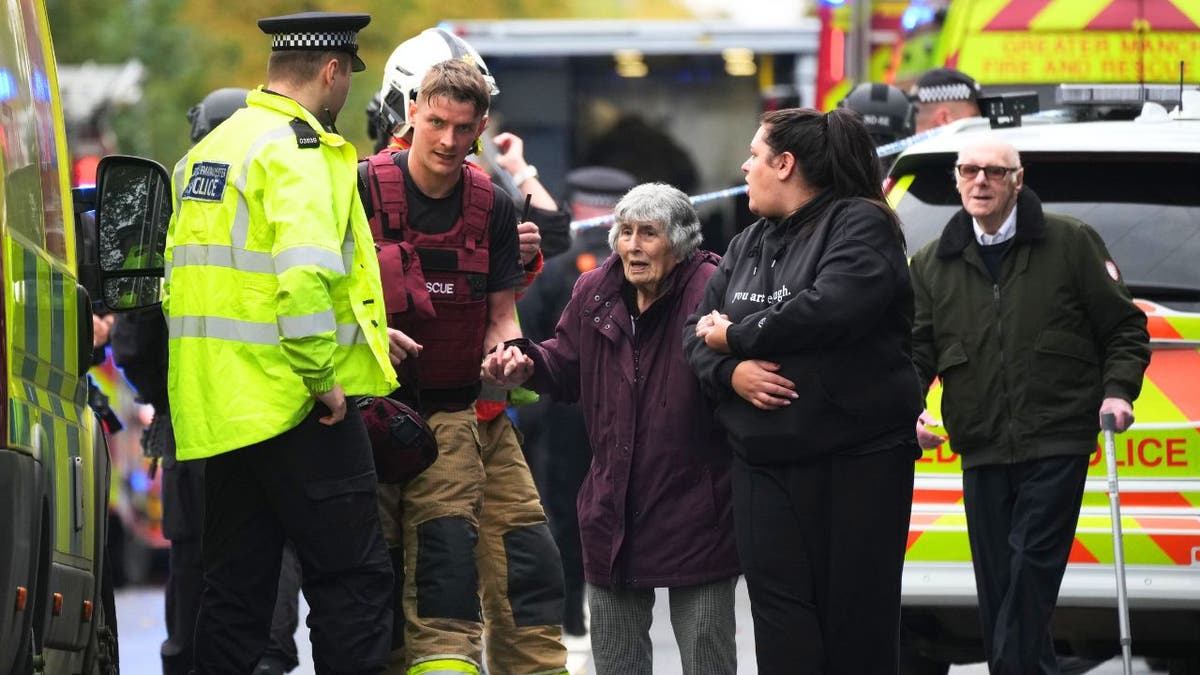 Rescuers and police escort elderly woman and others after synagogue terror attack in Manchester.