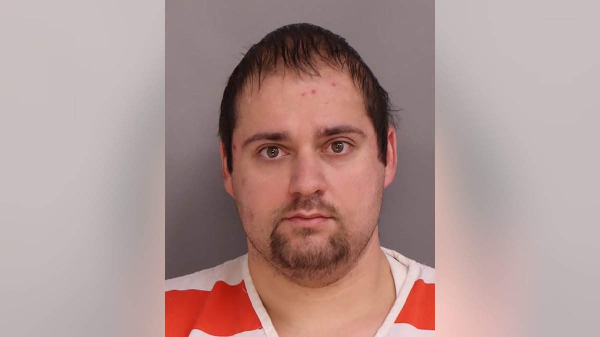 Justin Rutherford wearing a white and orange jumpsuit in his mugshot.