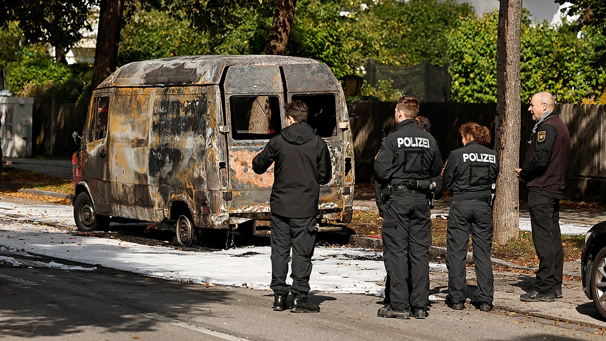 Police officers standing by a burnt van