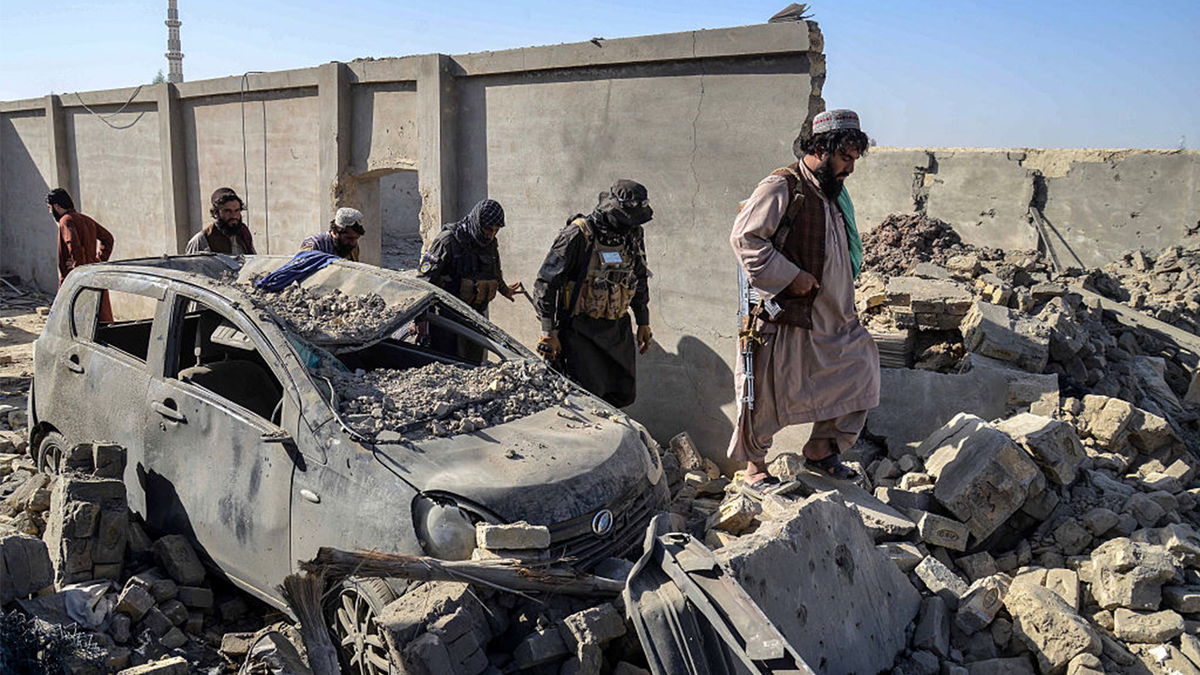 Taliban security personnel walk past a damaged car