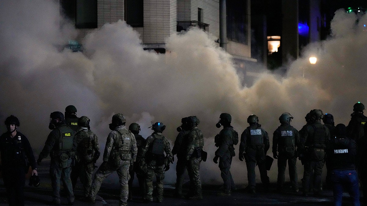 Law enforcement stand in front of tear gas cloud
