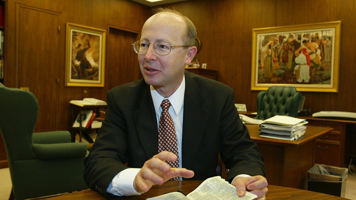 Richard Turley in a suit speaking as he holds a bible.