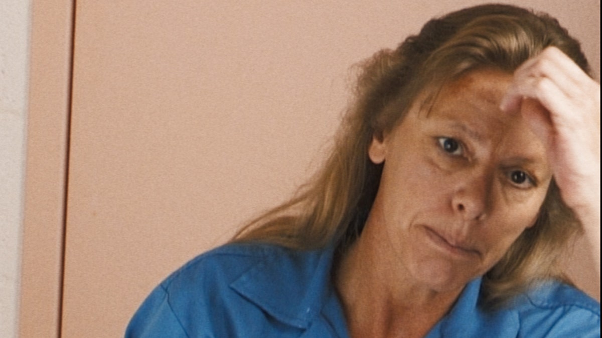 A close-up of Aileen Wuornos looking serious in a blue jumpsuit.