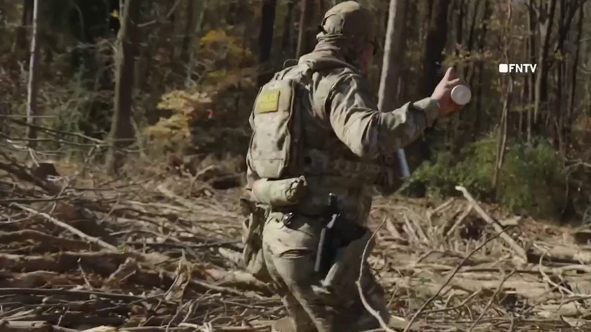 A Border Patrol agent wearing gear holds a tear gas canister while walking through a wooded area scattered with branches during a Homeland Security operation in Charlotte, North Carolina, on Nov. 16, 2025.