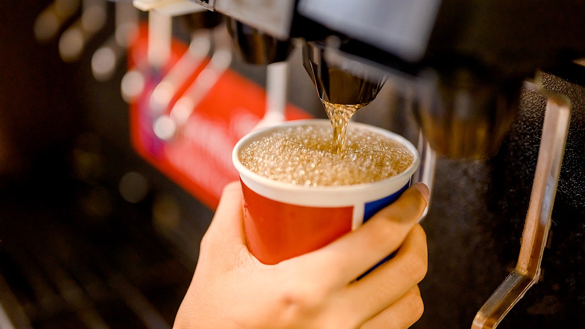 Man pours a soda into a paper cup at fountain machine.