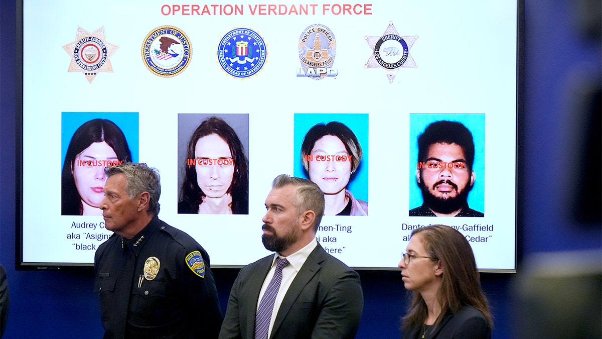 A display screen shows photos of several individuals during a law enforcement press briefing in Los Angeles.