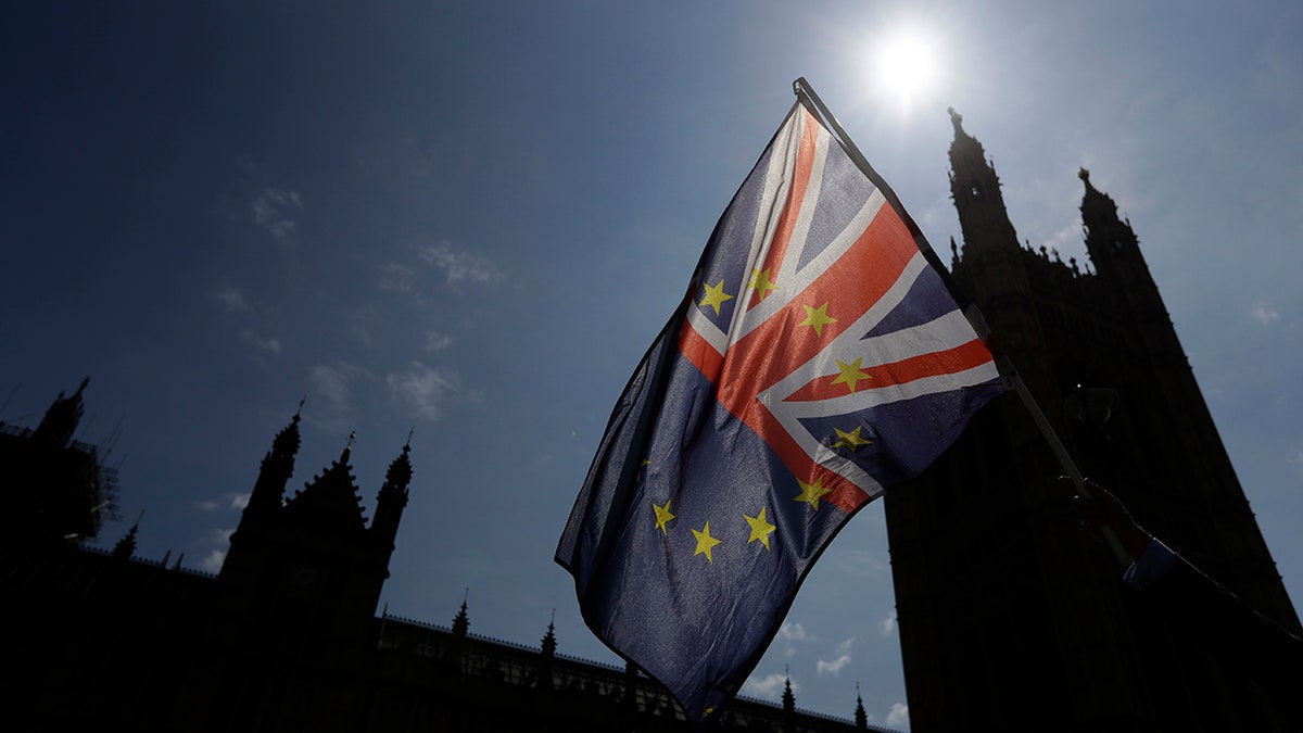 A flag is waved by a pro-EU demonstrator outside Parliament in London, Wednesday, June 13, 2018. The British government is bracing for more bruising debate on its key Brexit bill, after being forced to give ground to pro-EU lawmakers to avoid defeat.(AP Photo/Kirsty Wigglesworth)