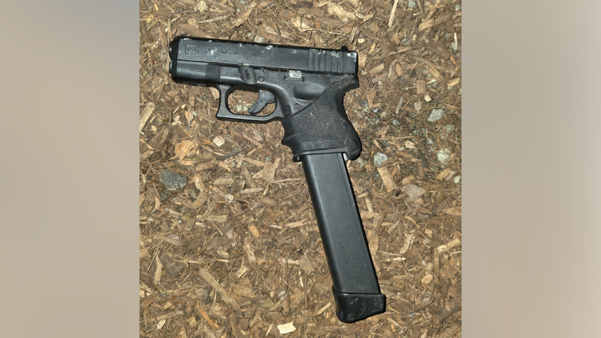 A handgun with an extended magazine lies on the ground