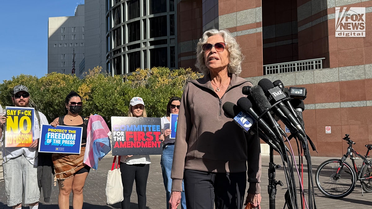 Jane Fonda speaking into a group of microphones held by members of the media.