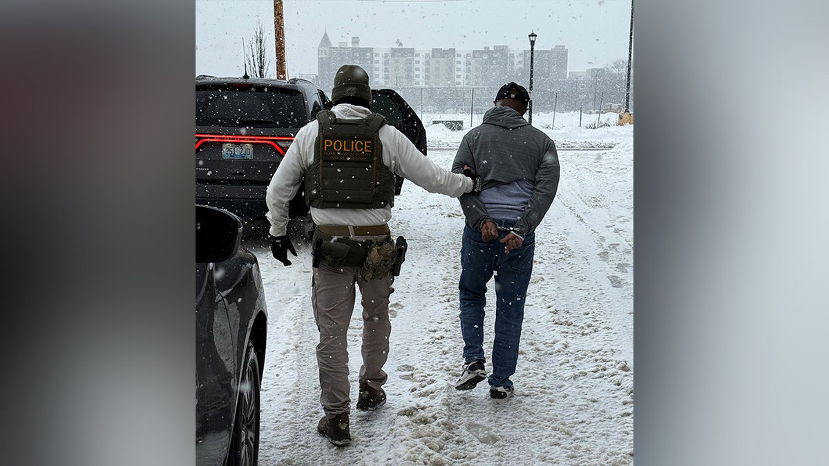 An officer walks next to Mahad Abdulkadir Yusuf, who is handcuffed
