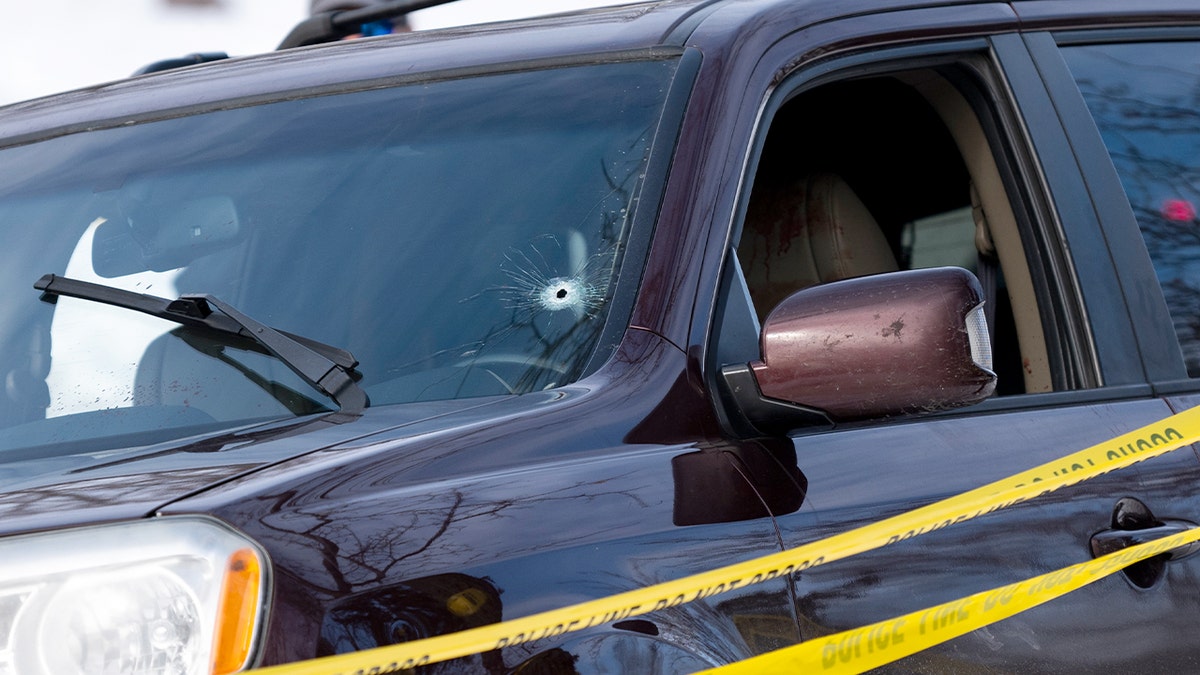 Damage from gunfire is visible on a vehicle’s front window during a federal law enforcement response.