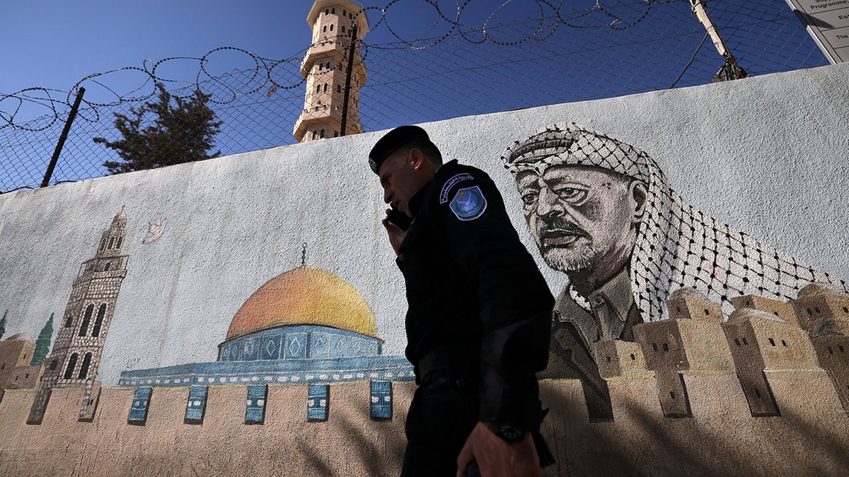 A Palestinian Authority policeman walks outside a police station adorned with a painting depicting late Palestinian leader Yasser Arafat, in the West Bank city of Hebron, on November 11, 2024, during the 20th anniversary of Arafat's death, amid increased violence in Israeli-occupied Palestinian territory as the war between Israel and the Hamas movement continues in the Gaza Strip.