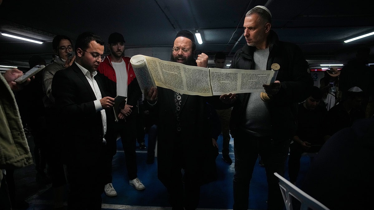 Jewish men reading from a scroll while seated in an underground parking garage.